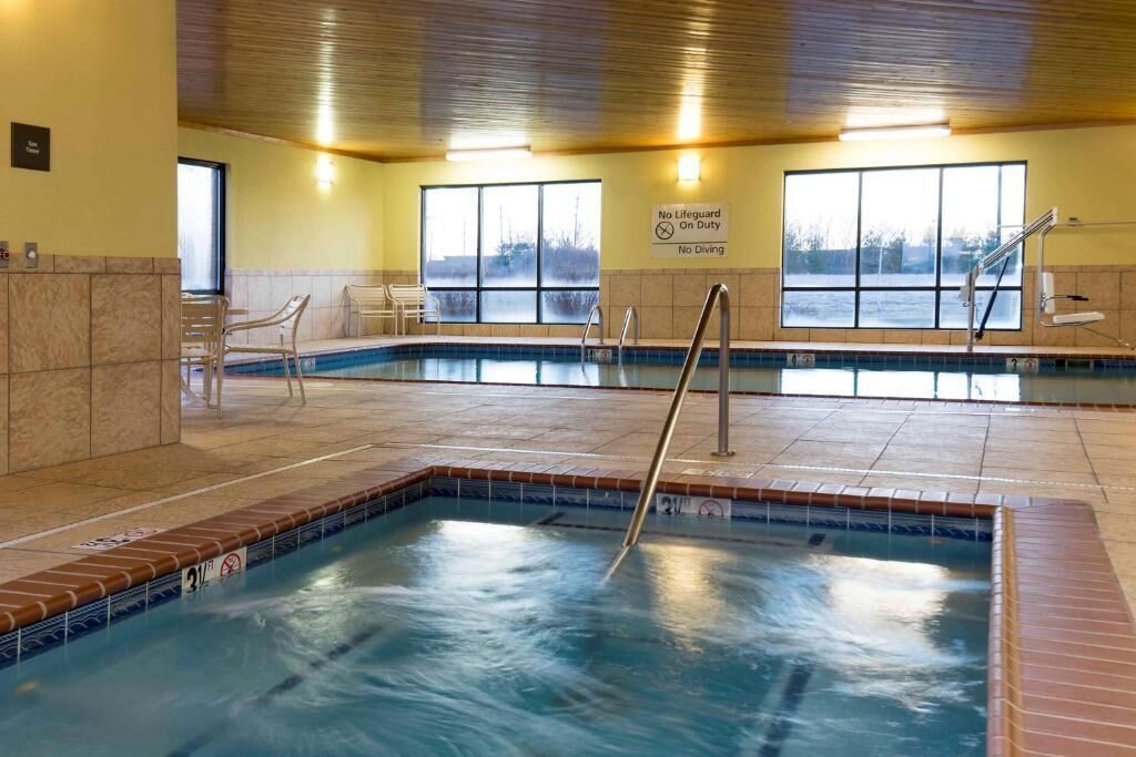 An indoor swimming pool with a no-lifeguard sign, tiled walls, and a view of the outdoors through large windows.