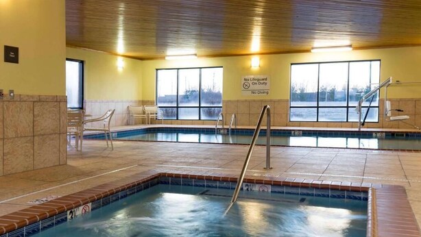 An indoor swimming pool with a no-lifeguard sign, tiled walls, and a view of the outdoors through large windows. - Hampton Inn & Suites LLC (Danville)