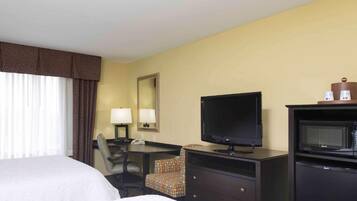 Une chambre d’hôtel comprenant un lit, un bureau avec une chaise, une télévision, un four à micro-ondes et un miroir au mur.