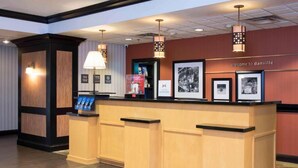 A reception desk with a 'welcome to danville' sign, framed pictures on the wall, and a lamp above it. - Hampton Inn & Suites LLC (Danville)
