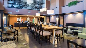 A hotel lobby with a long dining table, multiple chairs, a bar area, and a seating area with sofas and chairs. - Hampton Inn & Suites LLC (Danville)