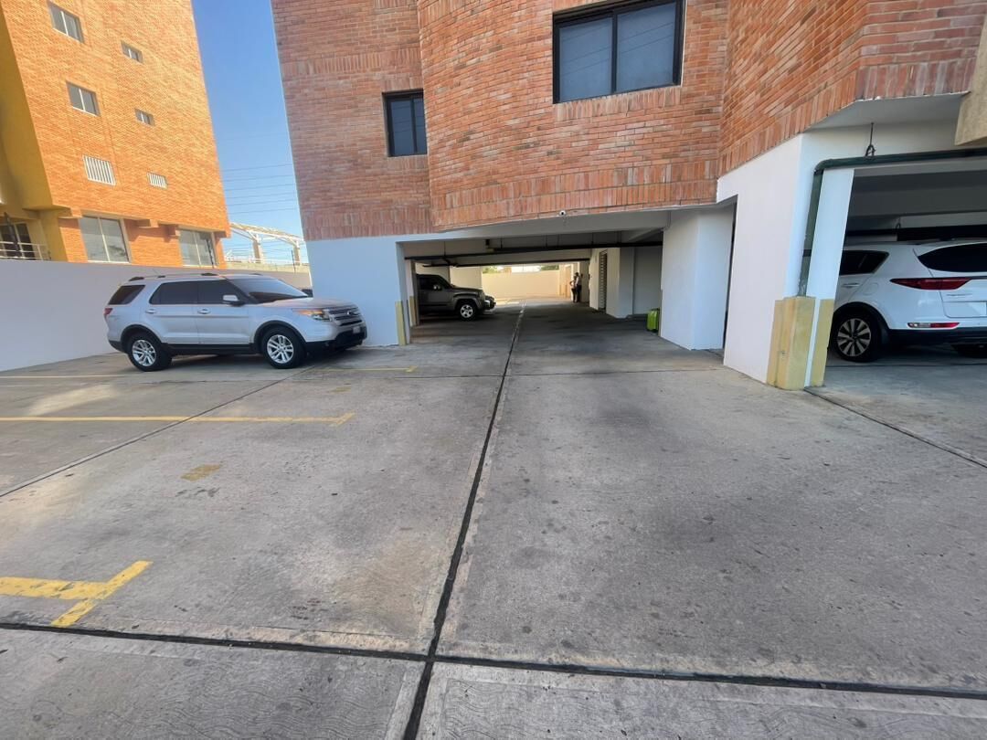 A parking garage with two cars parked, a brick building in the background, and a clear sky.