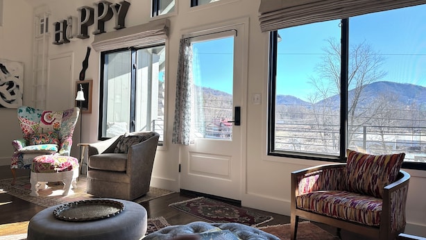 A spacious living room with large windows, a cozy fireplace, and a comfortable seating area. - Curious cottage with Mountain View’s in downtown Black Mountain (Asheville)