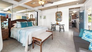 Un dormitorio amplio con una cama grande, un banco de madera, un rincón de comedor y una cocina visible a través de una puerta abierta.