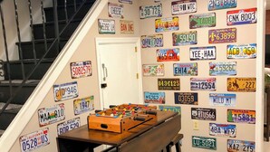Una habitación con una mesa de madera y taburetes, una mesa de fútbol y una pared decorada con numerosas placas de estado.