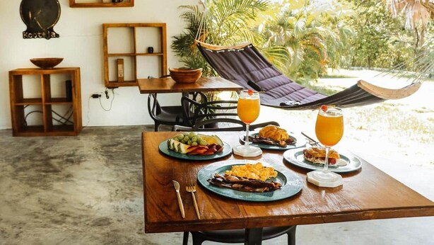 A dining table with plates of food and drinks, a hammock, and a view of greenery. - Aurora: Coronado, Private Paradise in Coronado Pool, Garden & Sun Terrace (Las Lajas)