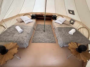 A tented room with two beds, each with a pillow labeled 'Kooteja,' a small rug, and wooden furniture.