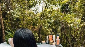 A person relaxing in a hot tub surrounded by candles and greenery.