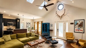 A spacious living area with a green sofa, leather ottomans, a blue cabinet, and a ceiling fan. - Modern Farmhouse Retreat Minutes to Tryon International + Wineries (Rutherfordton)
