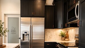 A modern kitchen with dark cabinetry, stainless steel appliances, and a marble countertop. - Modern Farmhouse Retreat Minutes to Tryon International + Wineries (Rutherfordton)