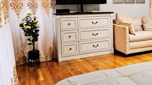 A bedroom with a bed, a dresser with drawers, a television on a stand, a sofa, and a small table with a vase of flowers.