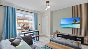 A modern living room with a large flat-screen TV, comfortable seating, and a view of the outside.