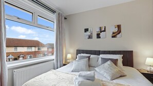 A hotel room with a large bed, a view of buildings outside, and three abstract paintings on the wall.