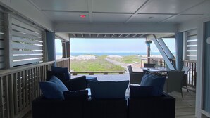 Een overdekt terras met rieten meubilair en uitzicht op het strand.