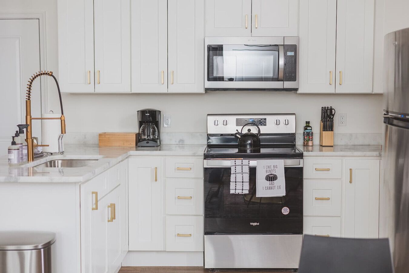 Una cocina moderna con armarios blancos, electrodomésticos de acero inoxidable y tiradores dorados.