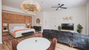 A modern bedroom with a brick wall, a bed, a TV, and a sofa. - Hillsborough Castle- Efficiency Suite (Martinsburg)