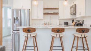 Een moderne keuken met een centraal eiland, roestvrijstalen apparatuur, houten stoelen en hanglampen.