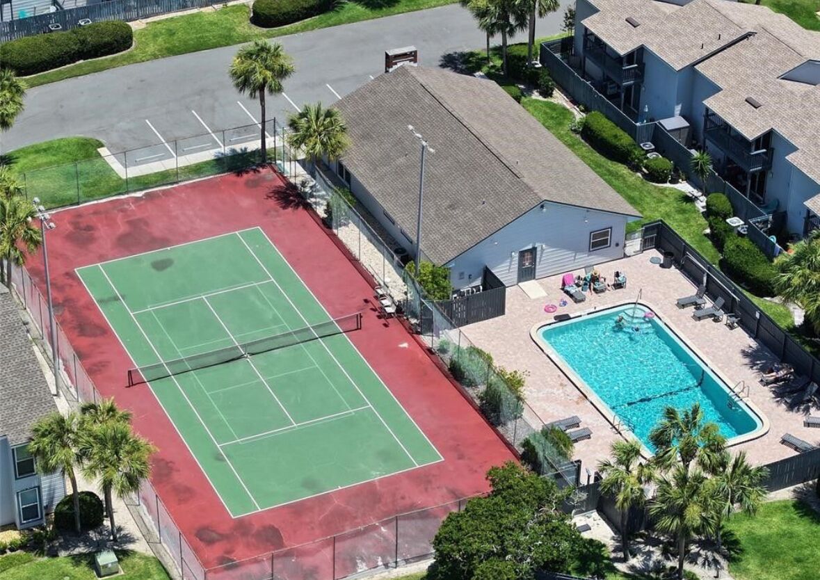 Luftaufnahme einer Wohngegend mit Tennisplatz, Schwimmbad und angrenzenden Häusern.