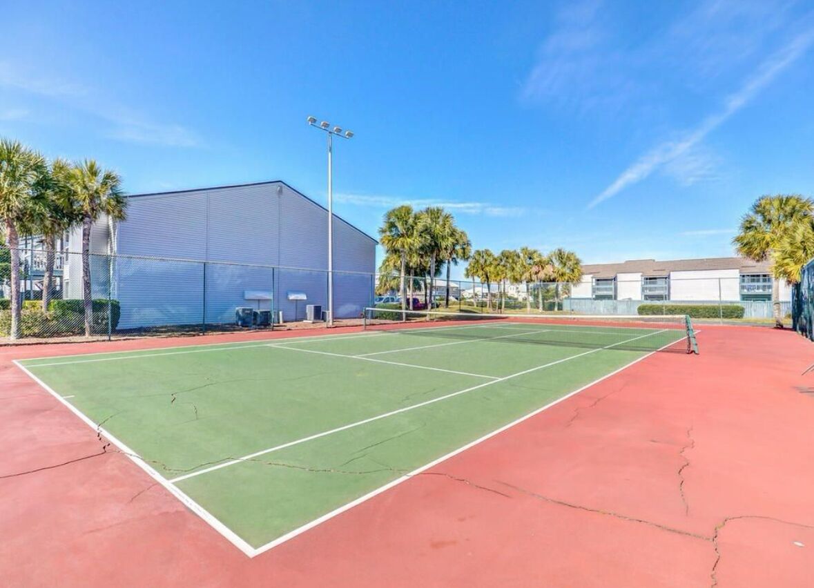 Un court de tennis en plein air, doté d’une surface rouge et verte, entouré d’une clôture et de palmiers.