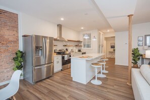 Une cuisine moderne dotée d’appareils électroménagers en acier inoxydable, d’un îlot central avec des tabourets et d’un mur décoratif en briques.