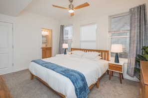 Une chambre à coucher avec un lit, des tables de chevet, un ventilateur de plafond et une fenêtre avec des rideaux.