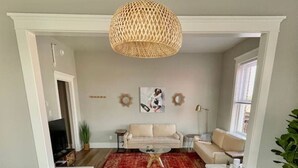 Un coin repas avec une table ronde blanche et des chaises, un tapis à motifs rouges et un luminaire suspendu en fibres tressées.