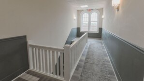 Un couloir avec une rambarde blanche, une moquette grise et une porte à deux battants avec des fenêtres au bout.