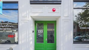Un immeuble avec une porte verte, le numéro 133, et un bouton d’alarme incendie rouge au-dessus.