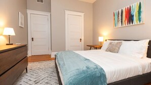 Une chambre à coucher comprenant un lit, deux tables de chevet, une commode et un tableau accroché au mur.