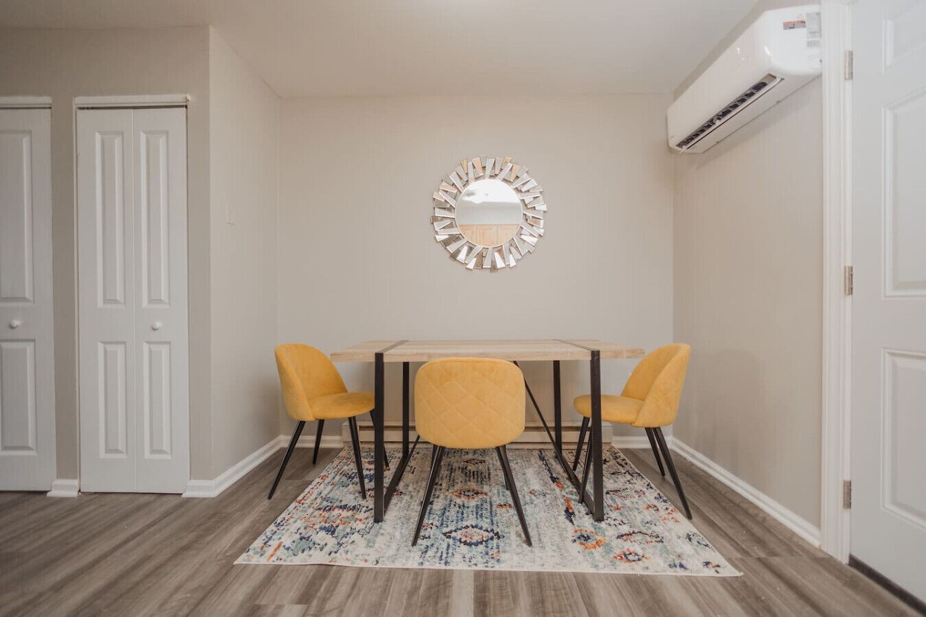 Un coin repas comprenant une table et deux chaises, un tapis à motifs et un appareil de climatisation.