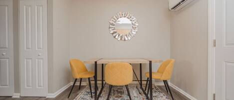Un coin repas comprenant une table et deux chaises, un tapis à motifs et un appareil de climatisation.