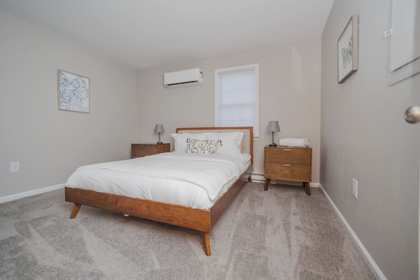 Un dormitorio con una cama de madera, dos mesitas de noche, aire acondicionado, una ventana y un cuadro en la pared.