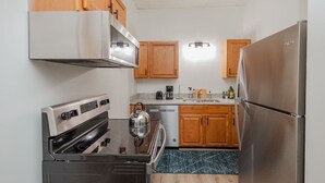 A compact kitchen with wooden cabinets, a stainless steel refrigerator, a gas stove, and a coffee maker. - The Radiant Residence (Martinsburg)