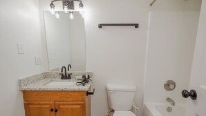 Un baño con tocador de madera, inodoro blanco, bañera y espejo con iluminación.