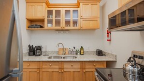 Cocina compacta con armarios de madera, pileta de acero inoxidable y estufa.