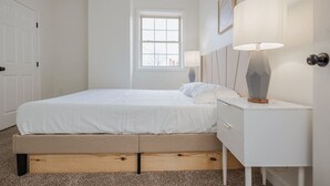 Un dormitorio con cama, mesitas de noche, una ventana y una puerta.