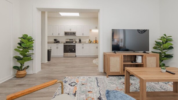 Ein modernes Wohnzimmer mit Fernseher, Holzmöbeln und einer Küche im Hintergrund.