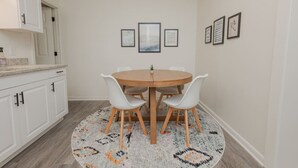 Ein Essbereich mit einem runden Holztisch, weißen Stühlen und einem gemusterten Teppich.