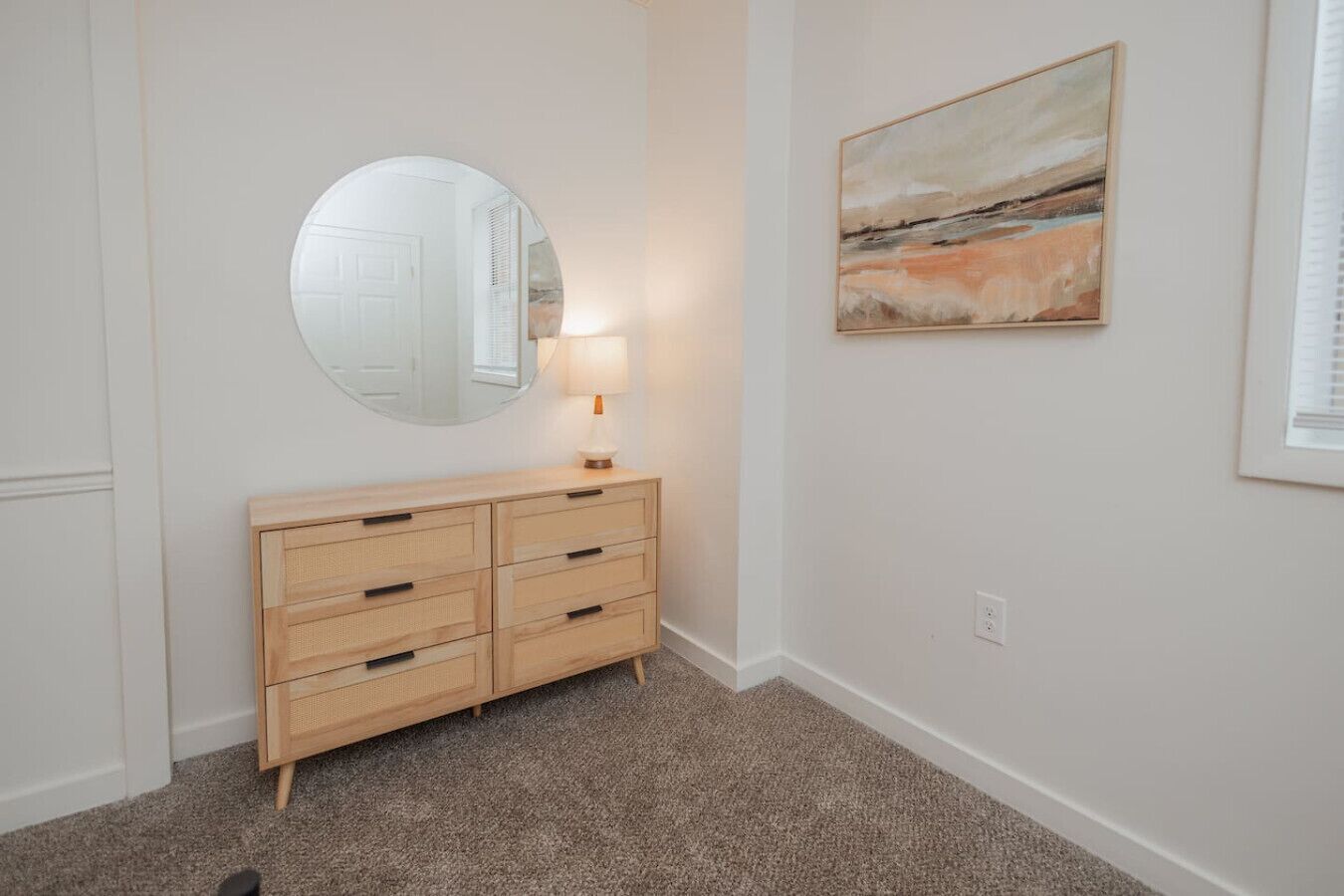 Una habitación con un aparador de madera, un espejo redondo y un cuadro en la pared.