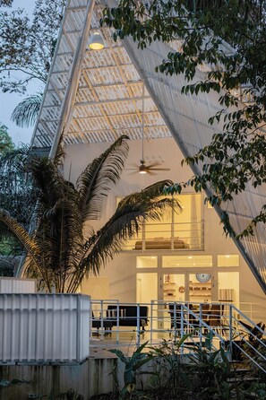 Una casa moderna con techo inclinado, ventanas grandes y una escalera que lleva a un balcón.