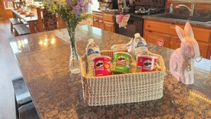 Una cocina con gabinetes de madera, encimera de granito, un florero con flores y una cesta con Pringles y una botella de agua.