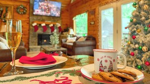 Una sala de estar acogedora con chimenea, un árbol de Navidad y un televisor mostrando una escena festiva.