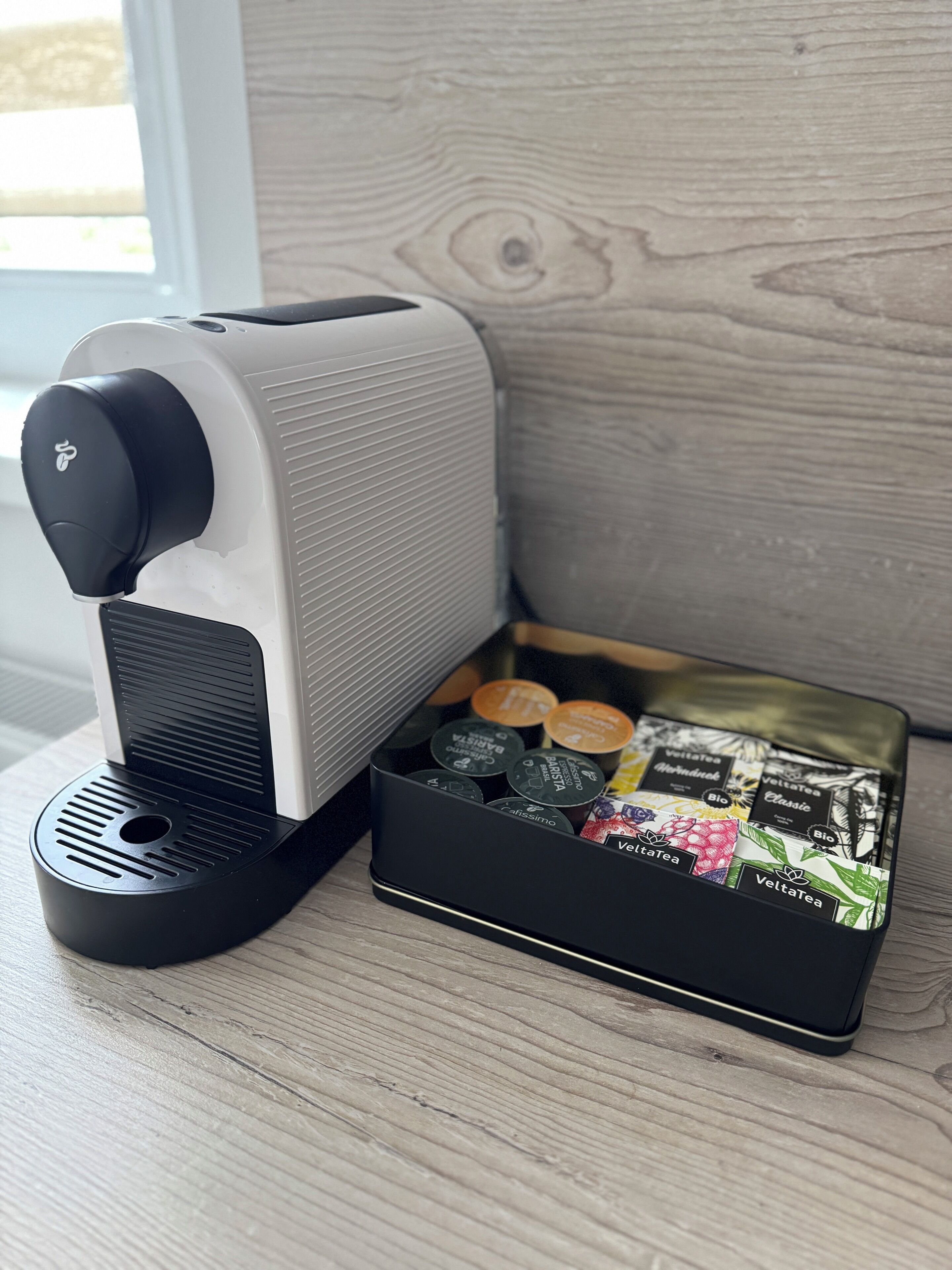 Eine Kaffeemaschine mit schwarz-weißem Design, schwarzem Fuß und einer Auswahl verschiedener Kaffeekapseln.