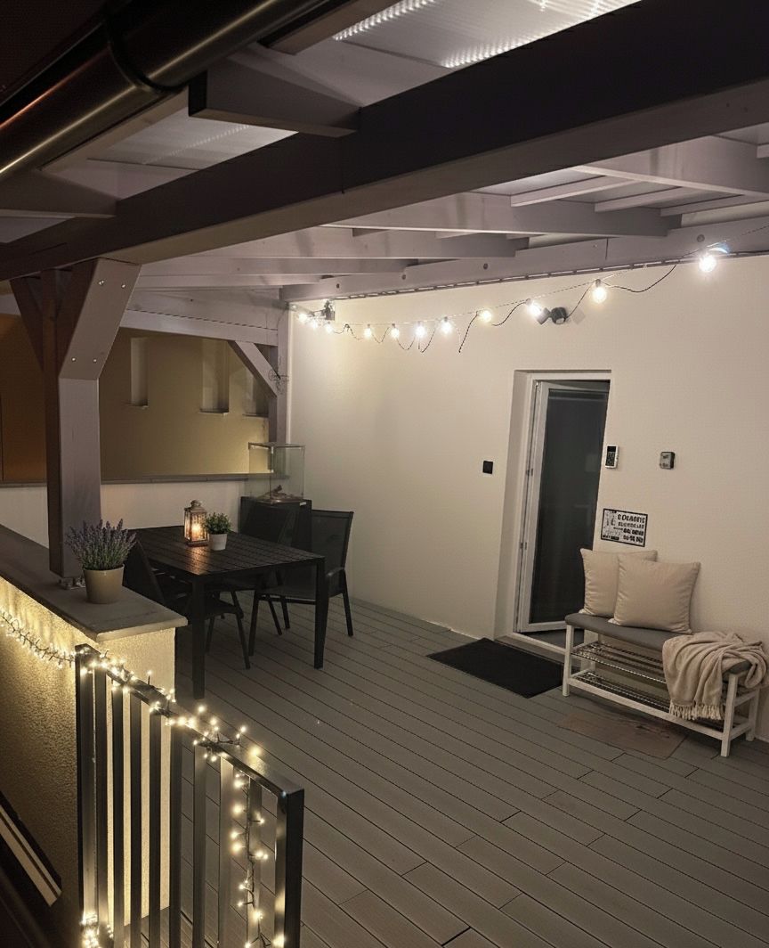 Un patio al aire libre con una mesa, sillas, un banco, luces colgantes y una puerta.