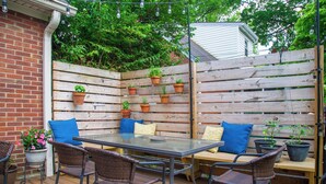 Eine Terrasse im Freien mit Holzzaun, Glastisch, Korbstühle und Blumentöpfen.