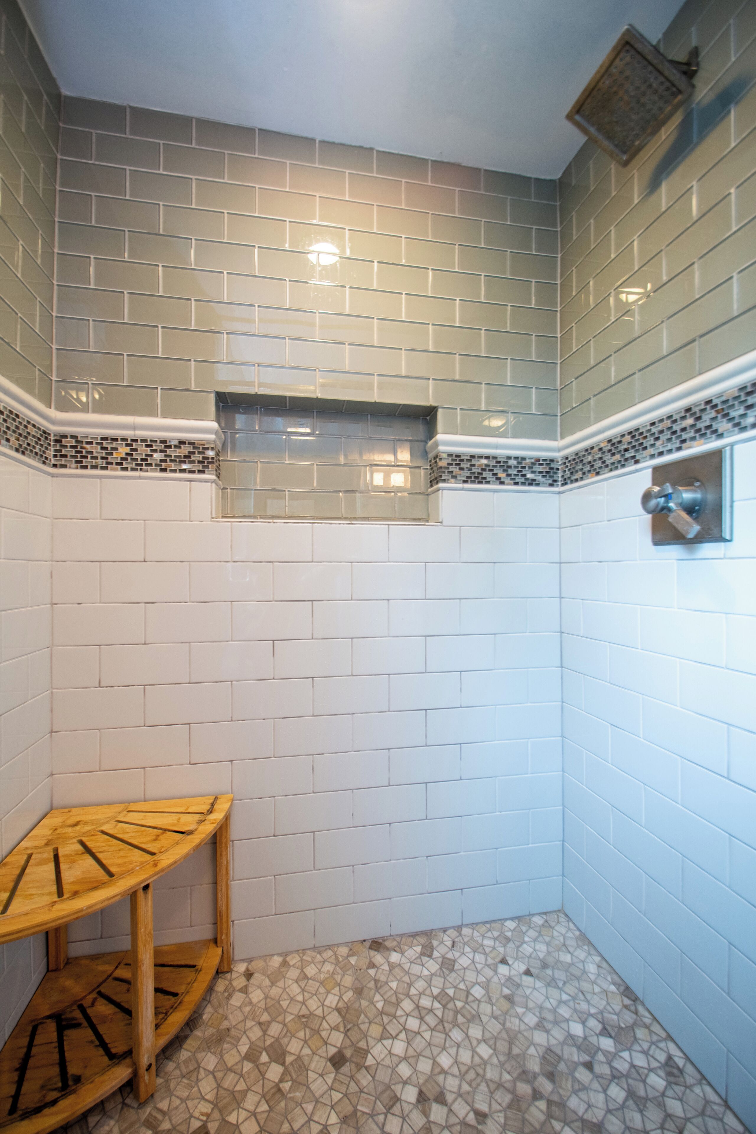 Un baño con azulejos blancos y grises, un estante de madera y una zona de ducha.
