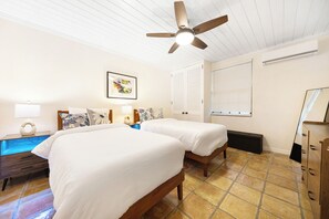 Ein Hotelzimmer mit zwei Betten, einem Deckenventilator, einem Nachttisch mit Lampe, einem Schminktisch und einem Fenster mit Jalousien.