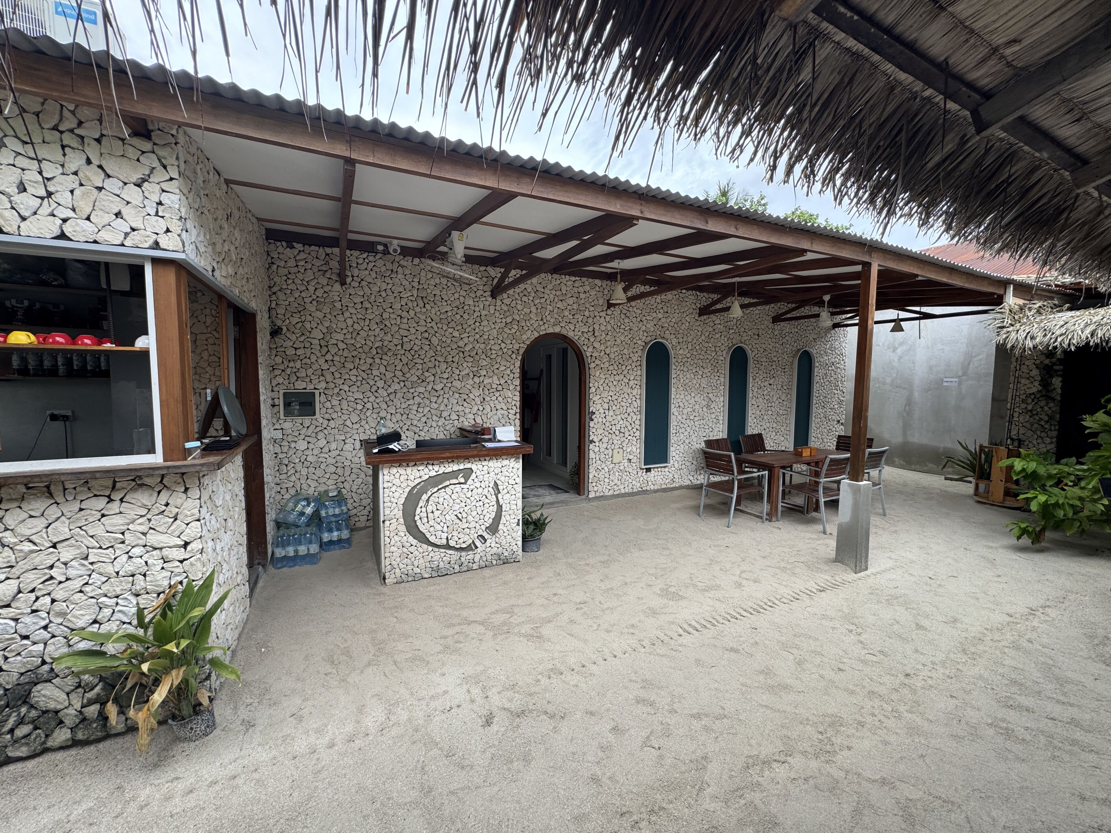 A covered outdoor area with a stone wall, a reception desk, and a seating area with tables and chairs.