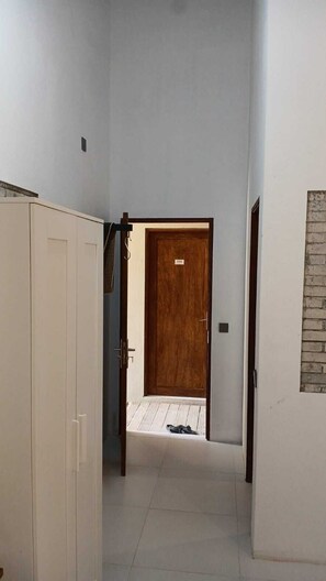 A hallway with a wooden door, a white wardrobe, and a tiled floor.