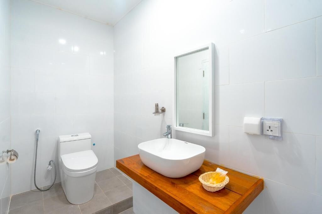 Un baño con inodoro blanco, lavamanos blanco sobre encimera de madera y un espejo sobre el lavamanos.